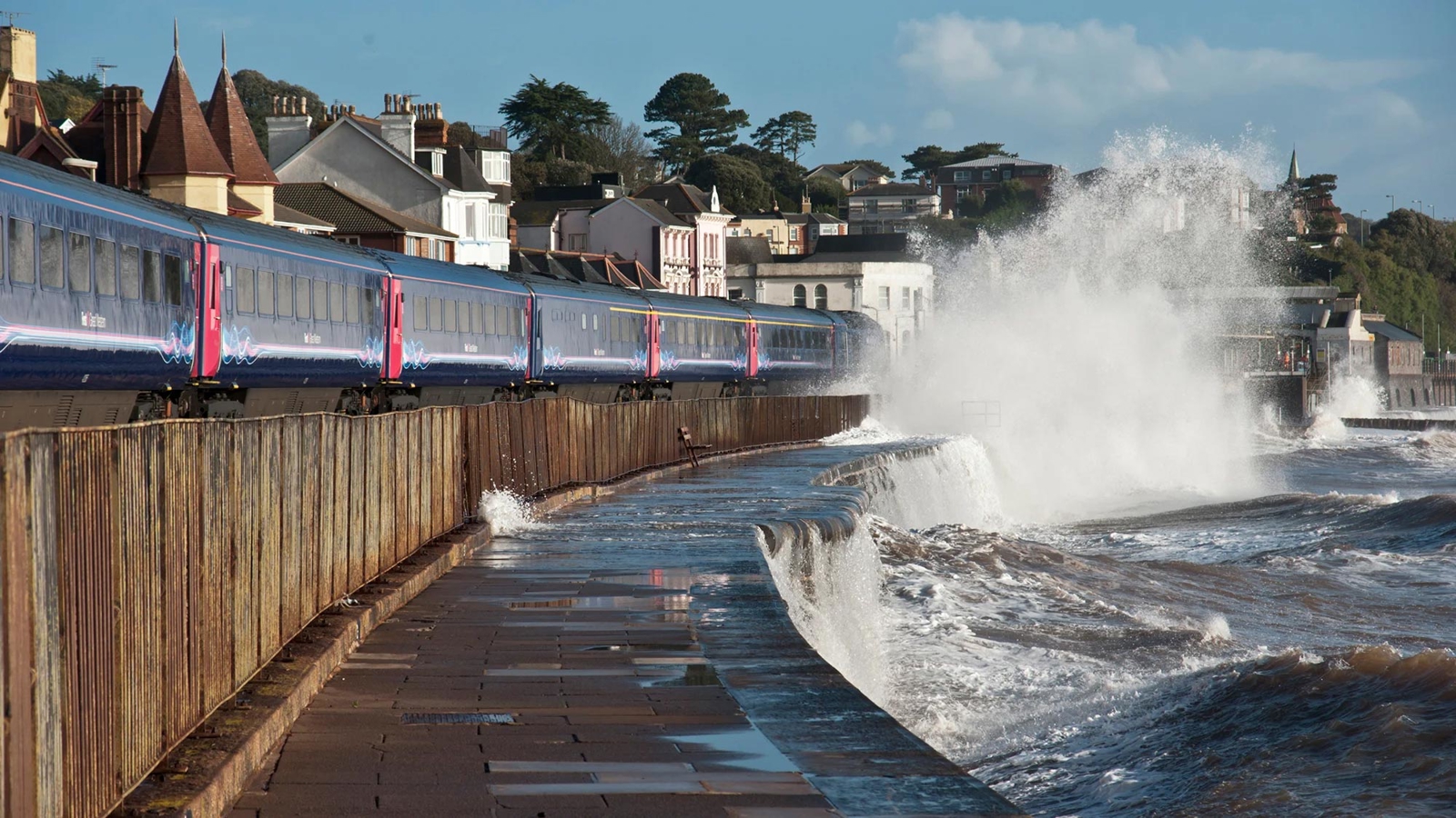 Train running along the coastline with waves throwing up water close to the track