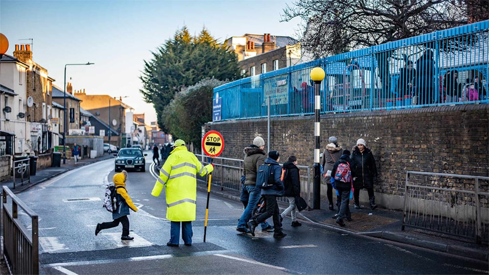 Children cross a road with a lollipop lady