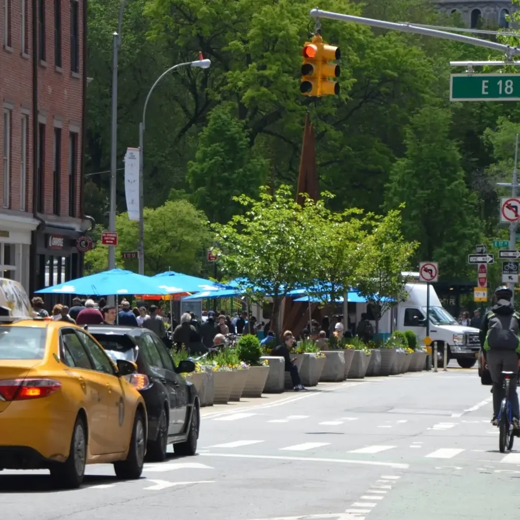 A yello taxi, cars and cyclists on a road in the US.