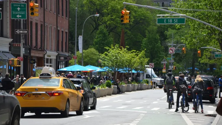 A yello taxi, cars and cyclists on a road in the US.