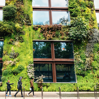 Building covered in plants on a street with pedestrians walking past