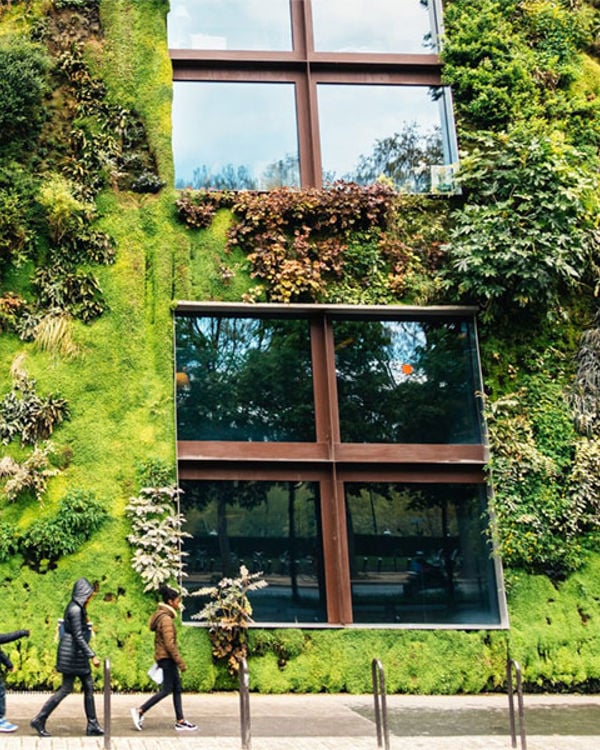 Building covered in plants on a street with pedestrians walking past