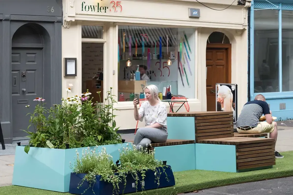 A lady taking a video call seated on a parklet in a London street