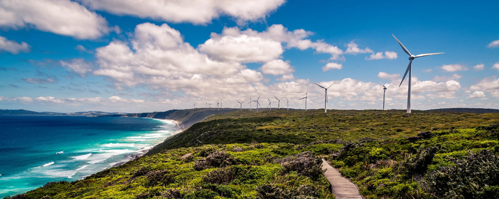 Ocean coast of Albany Western Australia with green scrub and wind turbines in the distance. Credit: Getty