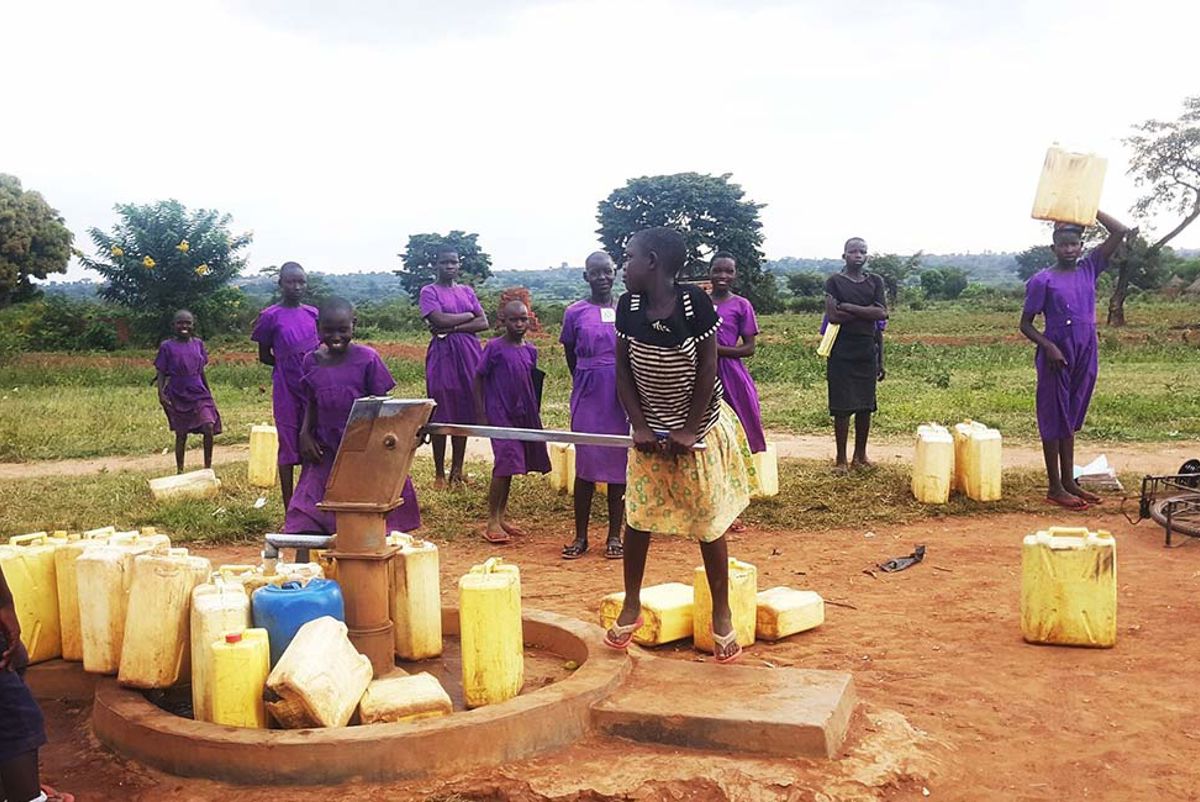 People using a handpump for water in Uganda, with containers lined up to fill with water