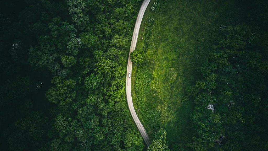 An aerial image of a forest, road and a car